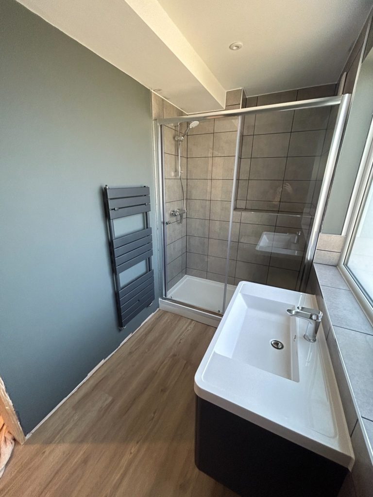 Bathroom renovation with new shower and screen, black radiator, vanity unit and toilet.